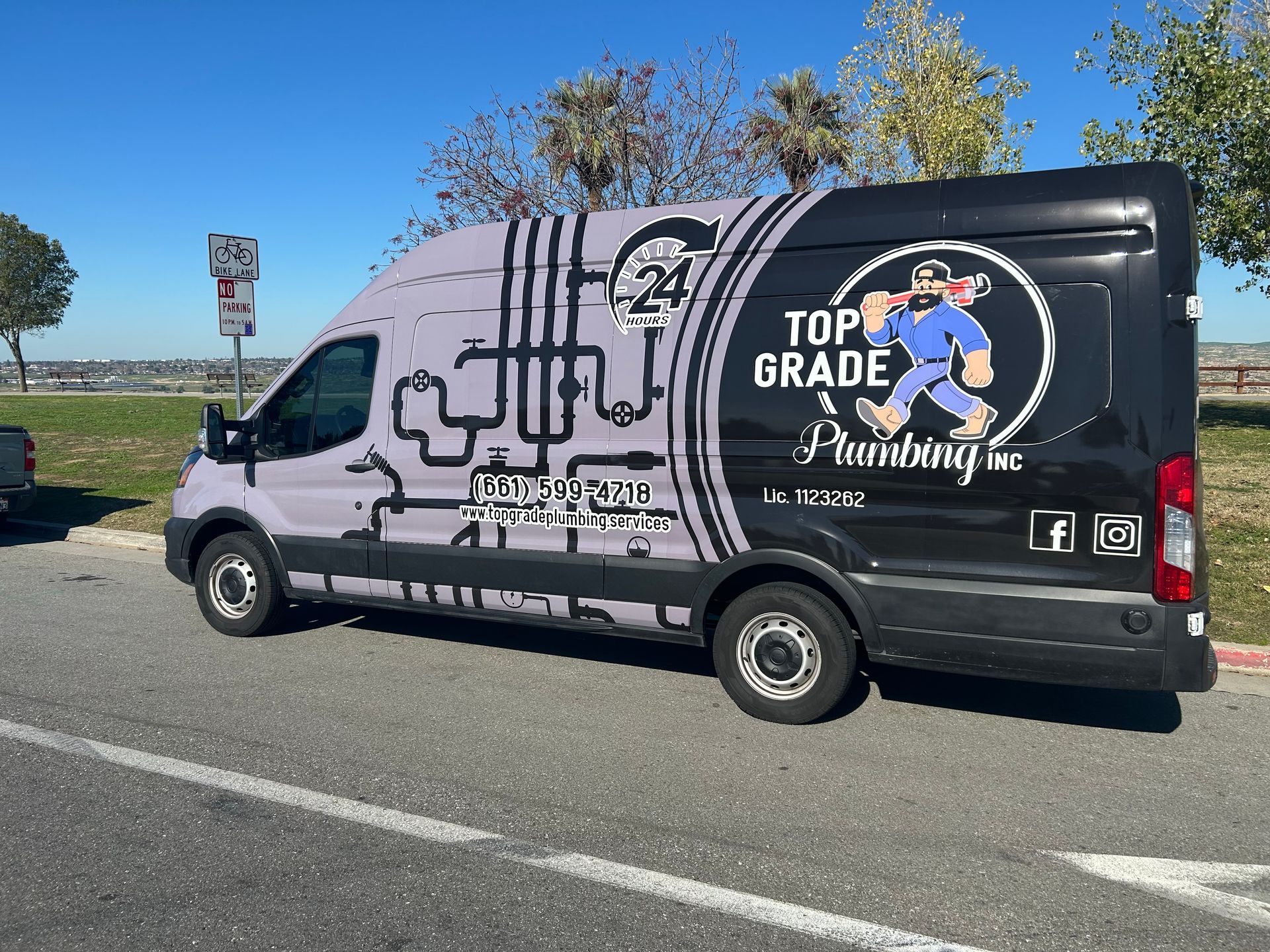 Black van with “4th Grade” graphics parked by a roadside under a blue sky.
