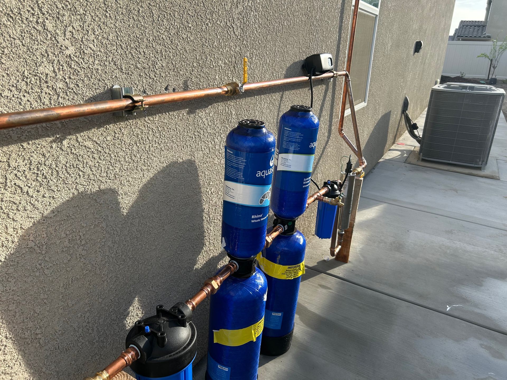 Stacked blue and yellow gas cylinders beside copper pipes along a building wall on a rooftop.