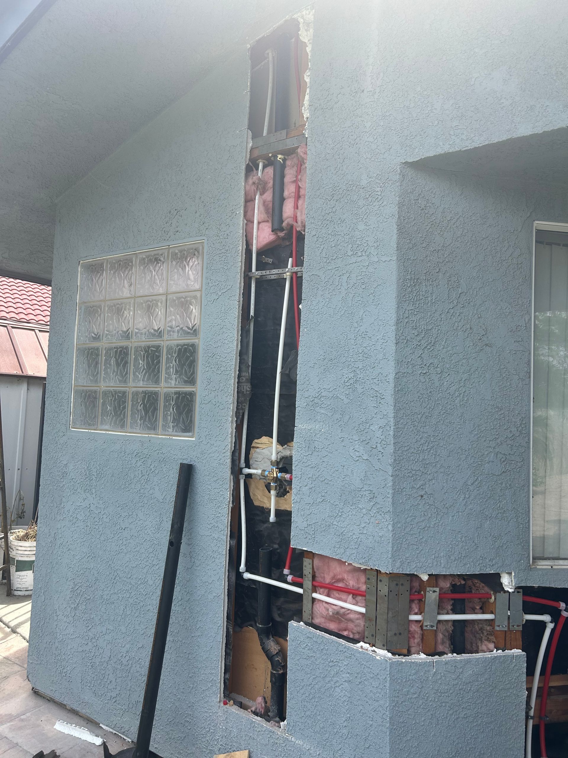Exterior house wall under construction with exposed framing, pipes, and a gray stucco finish