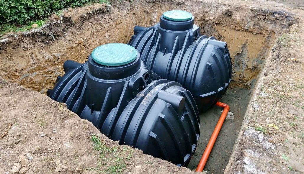 Two black underground tanks installed in a dirt excavation beside orange conduit tubing.