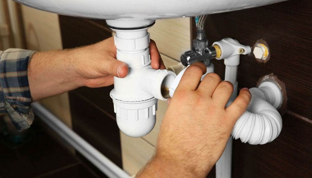 Hands tightening a white sink drain pipe under a bathroom sink
