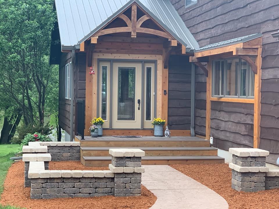 Brown house with a porch, steps, and a walkway. Brick walls flank the walkway.