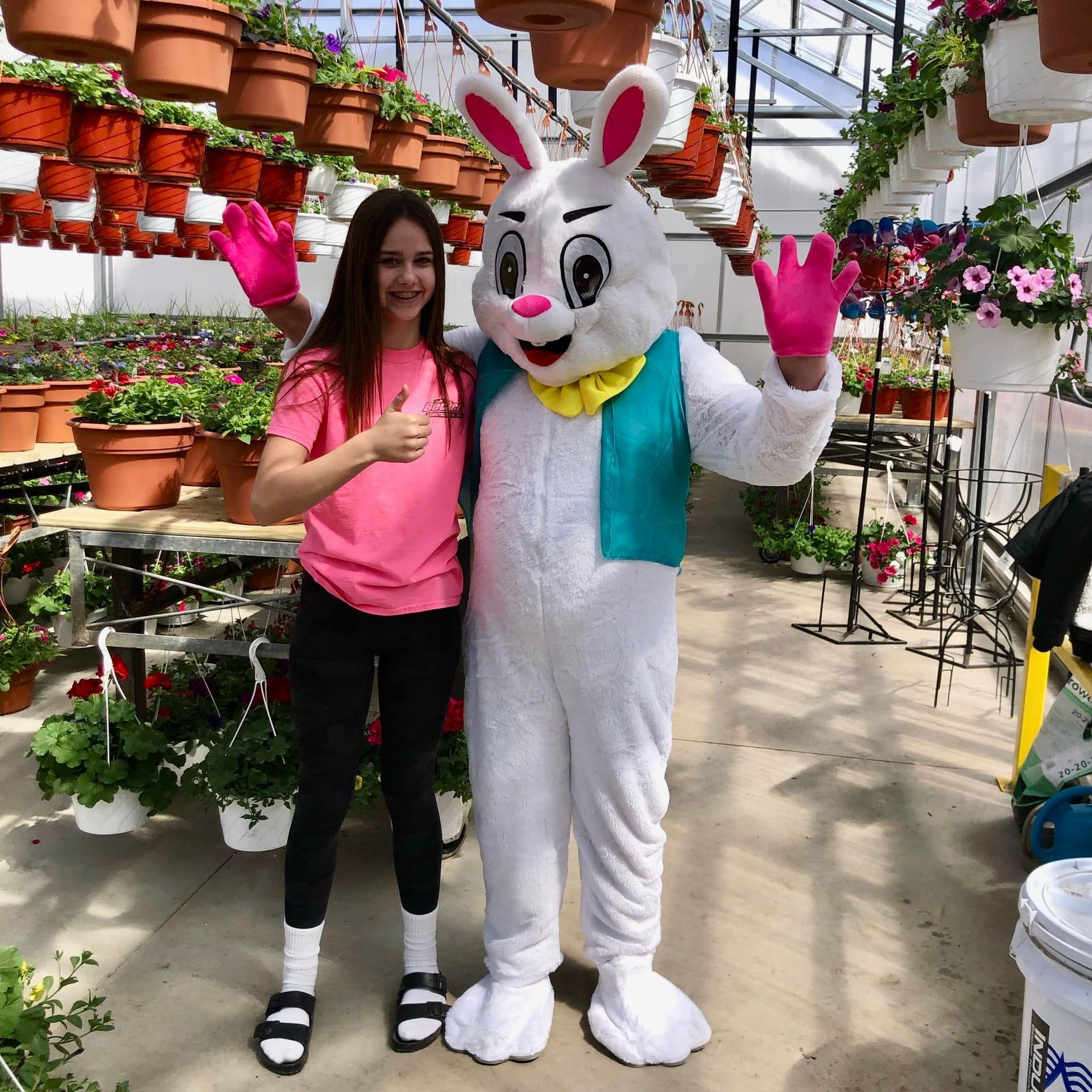 A girl is standing next to a bunny mascot in a greenhouse