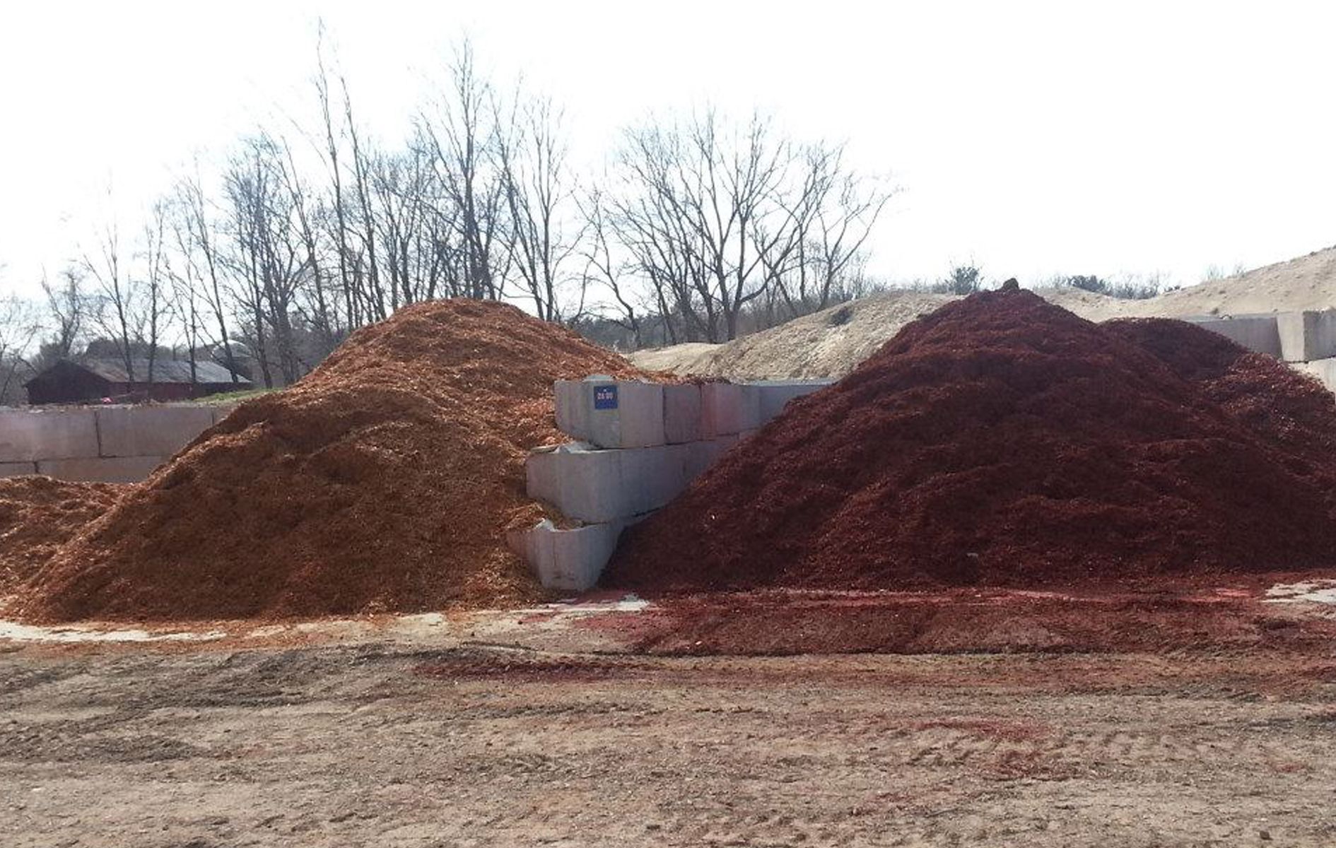 Two piles of wood mulch, one reddish-brown and one lighter brown, next to concrete blocks.