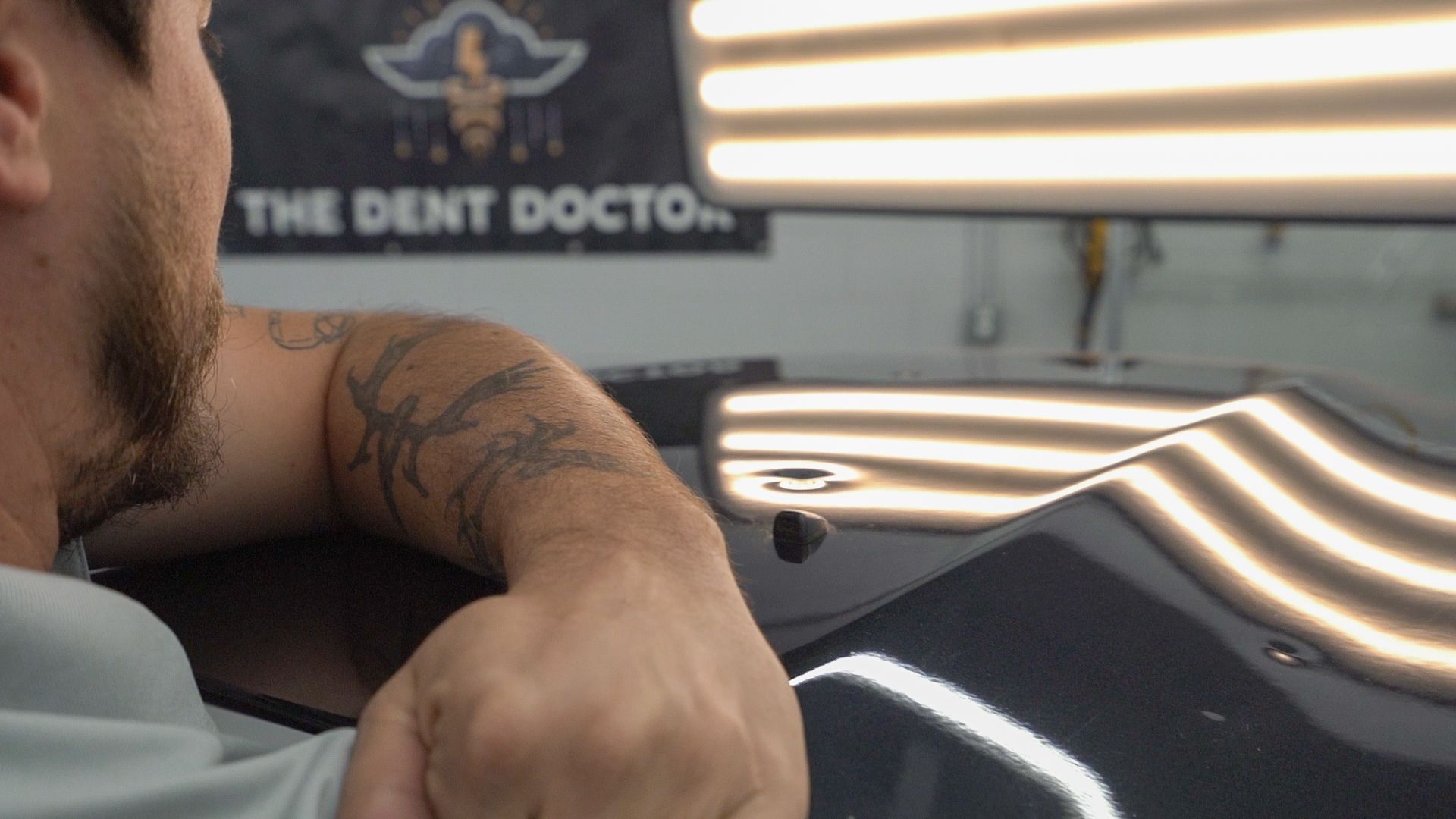 Man working on car's dent in a shop, using tools to repair a black car.