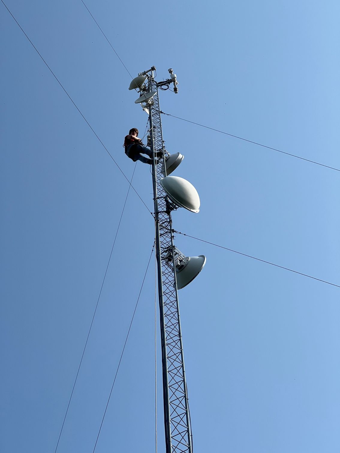A man is sitting on top of a telephone tower