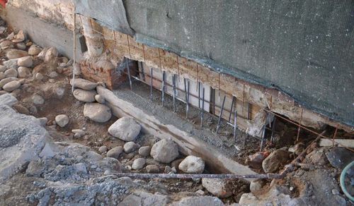 Exposed basement wall with window well, gravel, and rocks along the foundation.