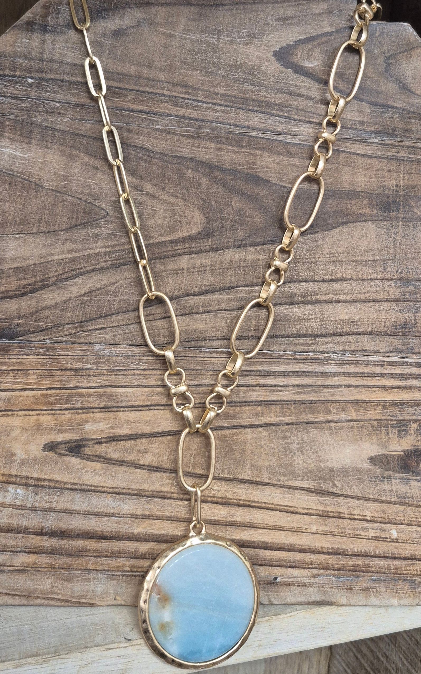 Gold necklace with a large, round, blue pendant, on a wooden surface.