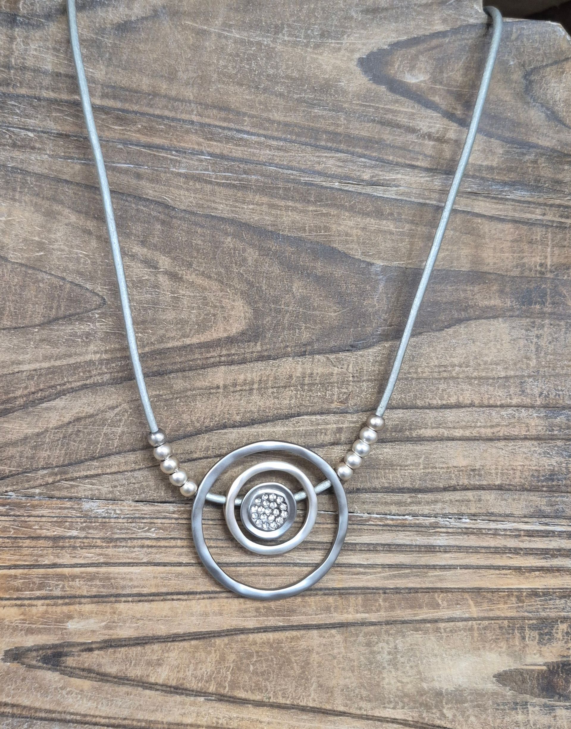 Silver necklace with circular pendant against a wooden background.