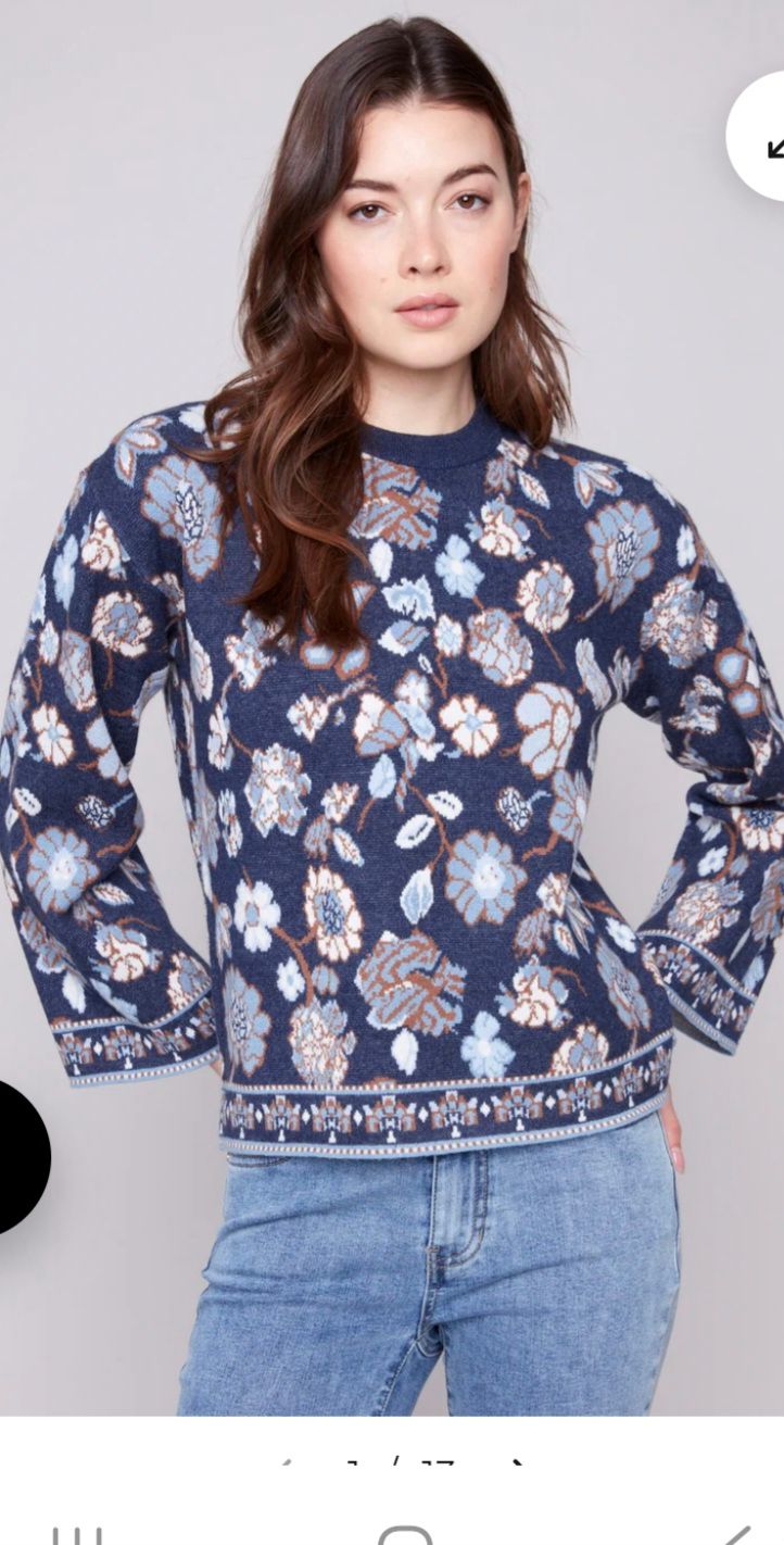 Woman wearing a navy blue floral sweater with flared sleeves, paired with jeans.