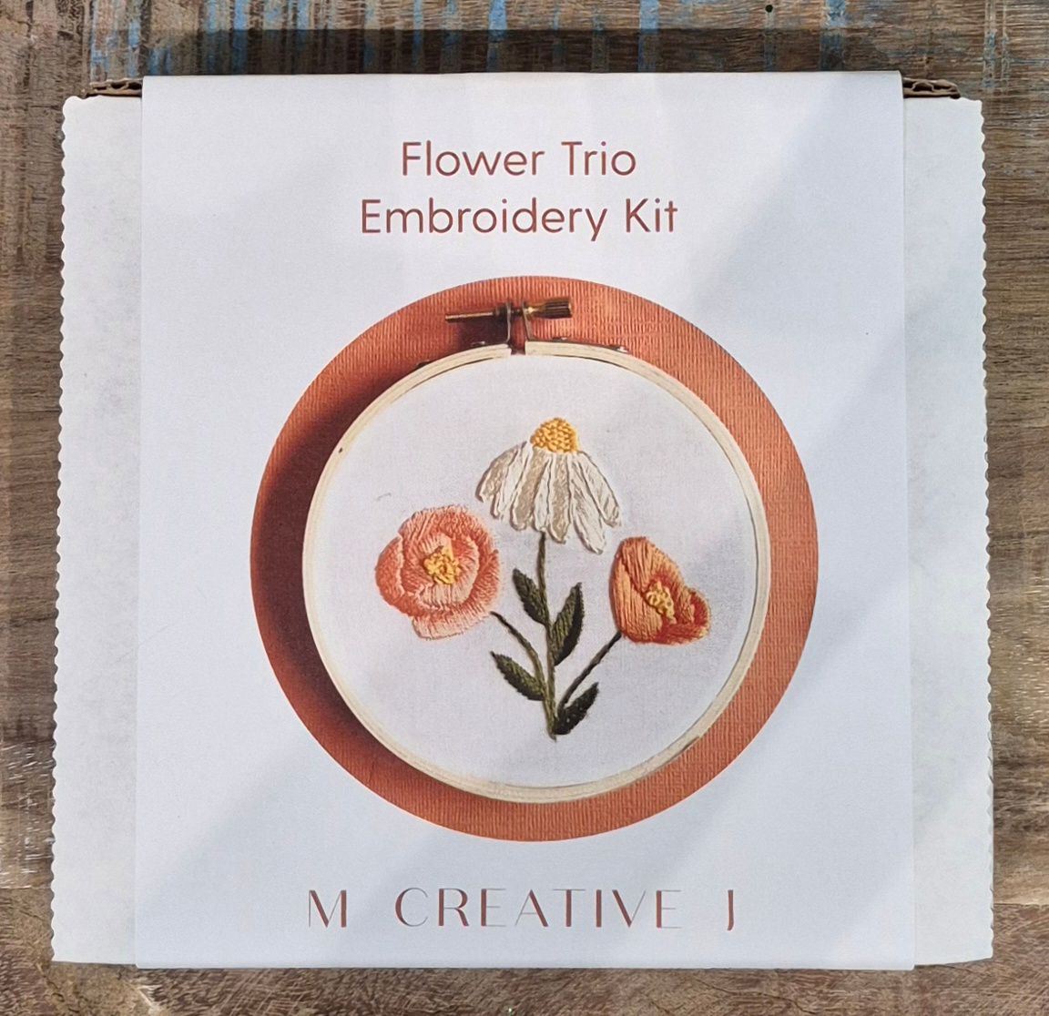 Embroidery kit with a floral design, featuring a daisy and two orange flowers.