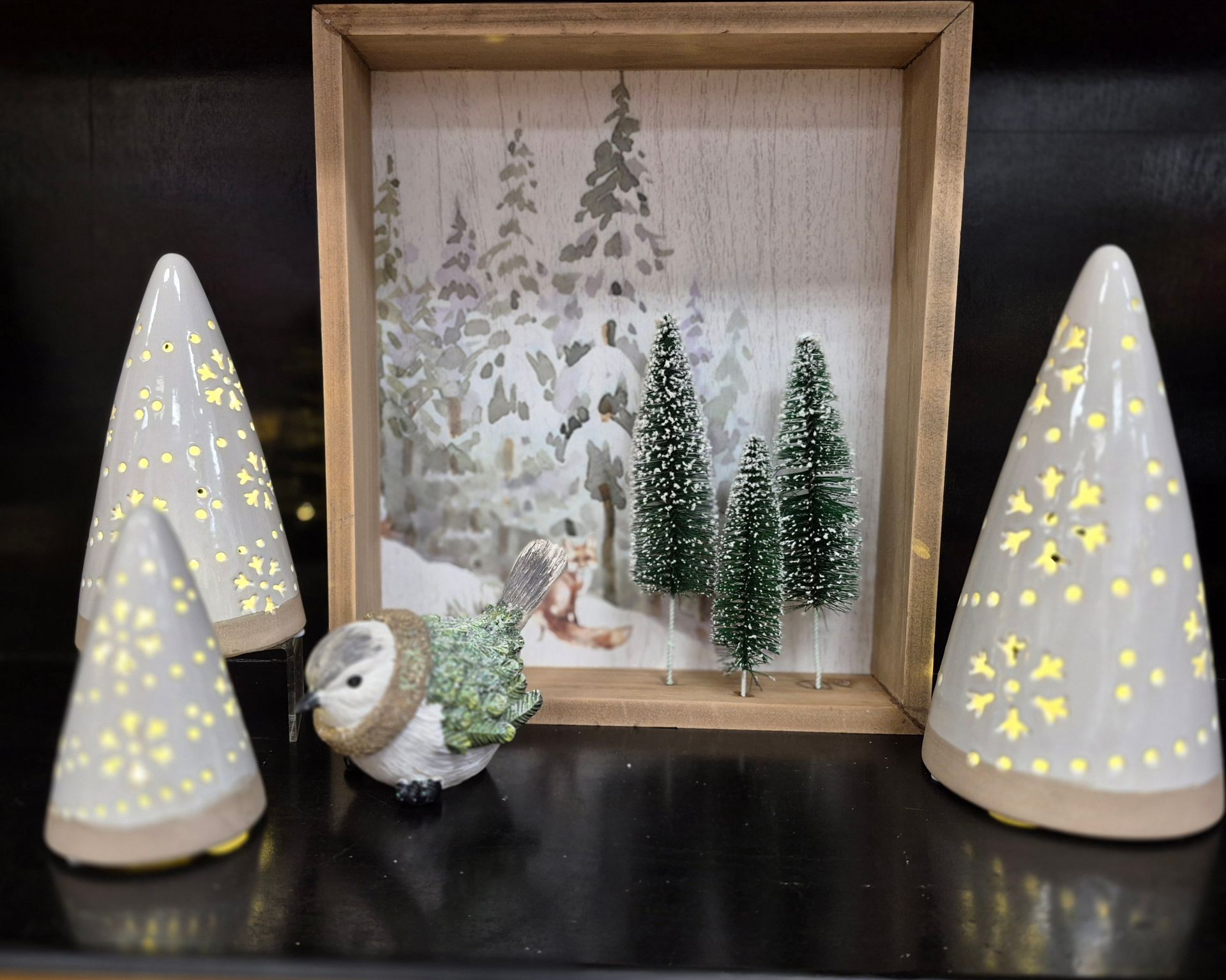 Winter scene: ceramic Christmas trees, snowy forest art, a bird, and miniature evergreen trees.