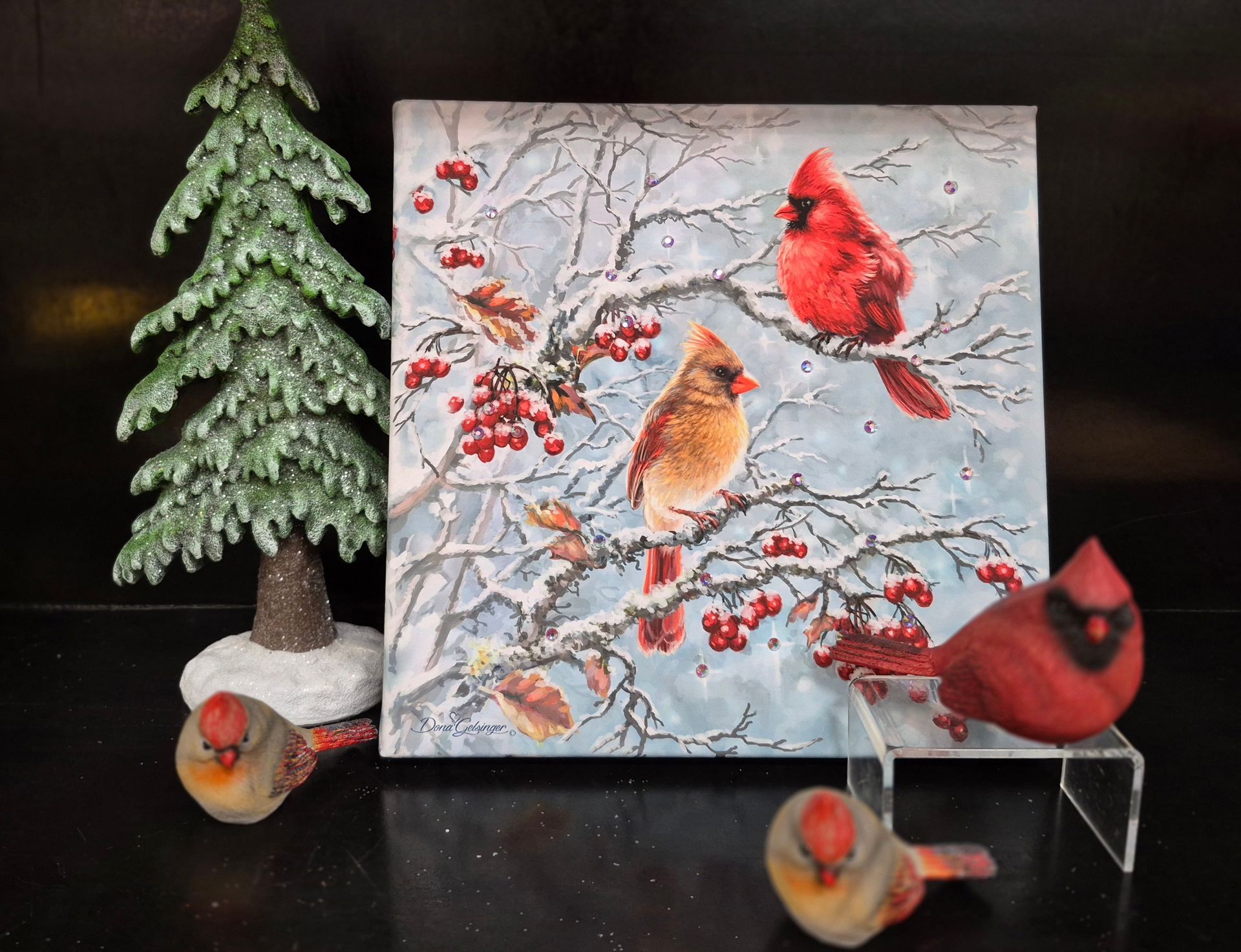 A painting of cardinals in a snowy tree with decorative cardinal figurines and a small Christmas tree.