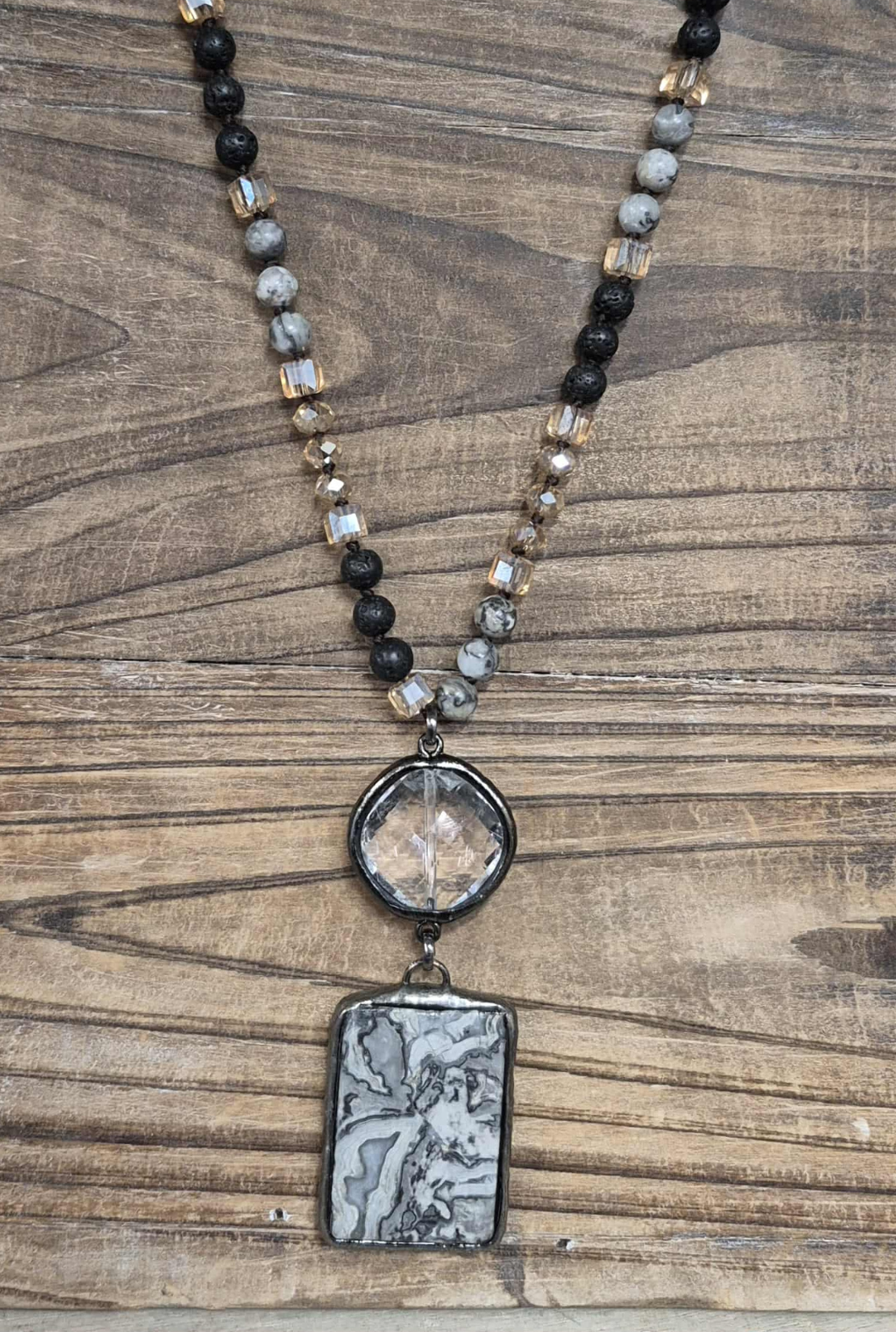 Beaded necklace with a pendant featuring a framed illustration on a wood grain surface.