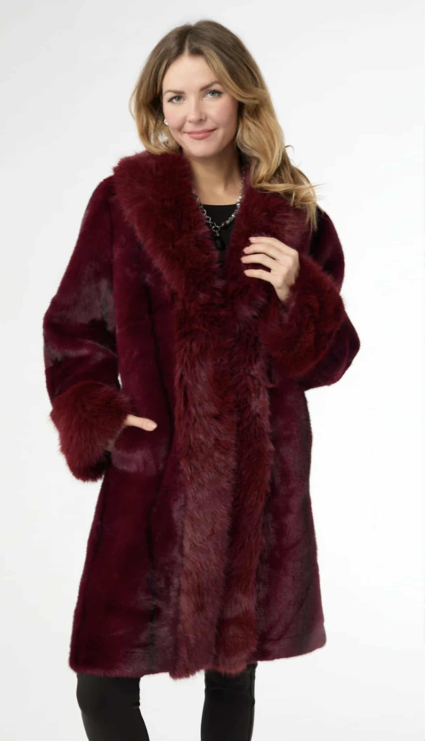 Woman in a burgundy fur coat, smiling, standing in a white studio.