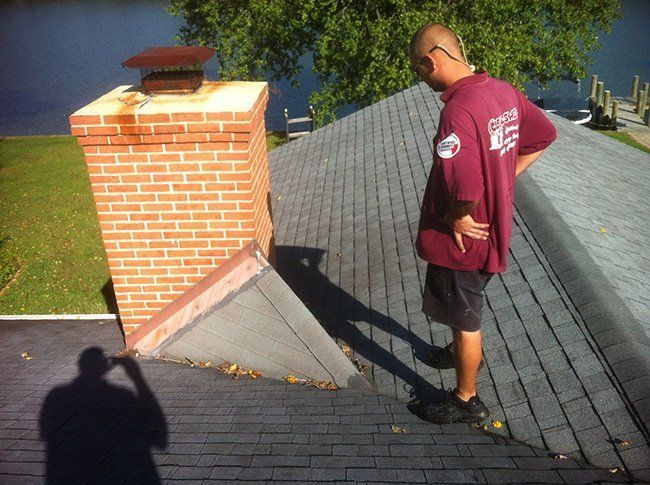 A man in a red shirt is standing on a roof next to a brick chimney.