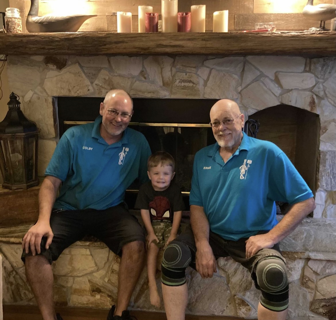 Two men and a child are sitting in front of a fireplace