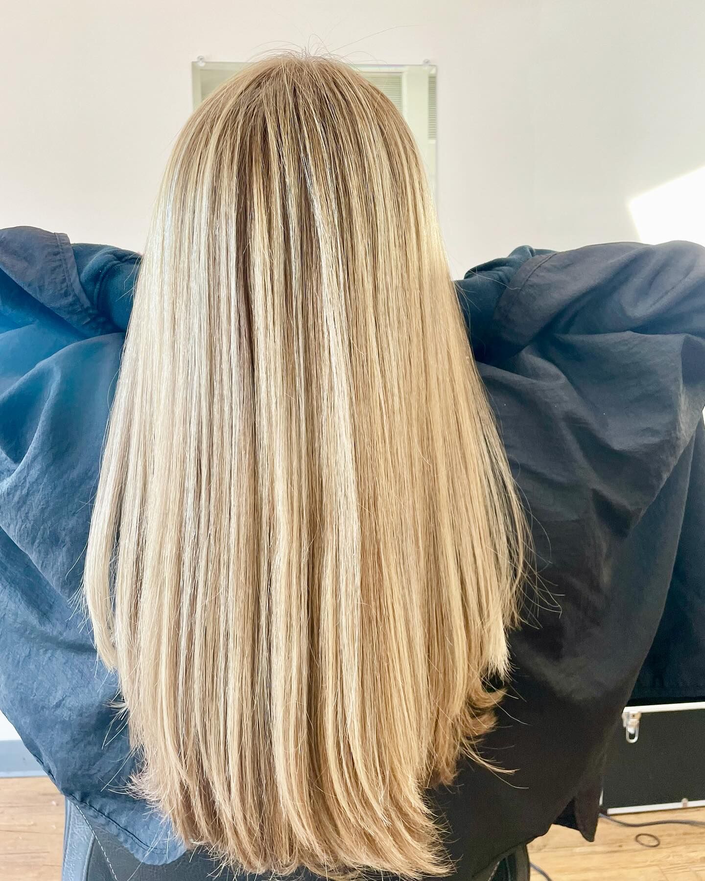 Blonde hair, styled straight, cascading down. Person in a black cape, indoors.