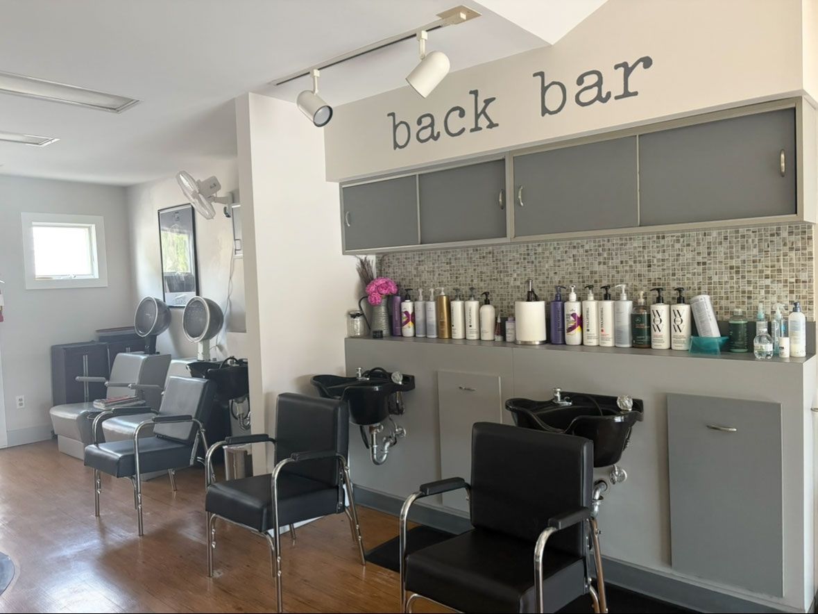 Salon back bar area with sinks, chairs, and product shelves