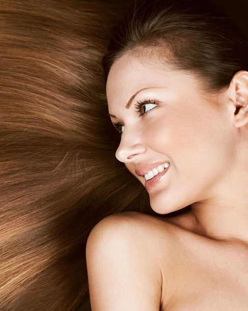 Woman with long, brown hair smiling, laying down. Bare shoulders, neutral background.
