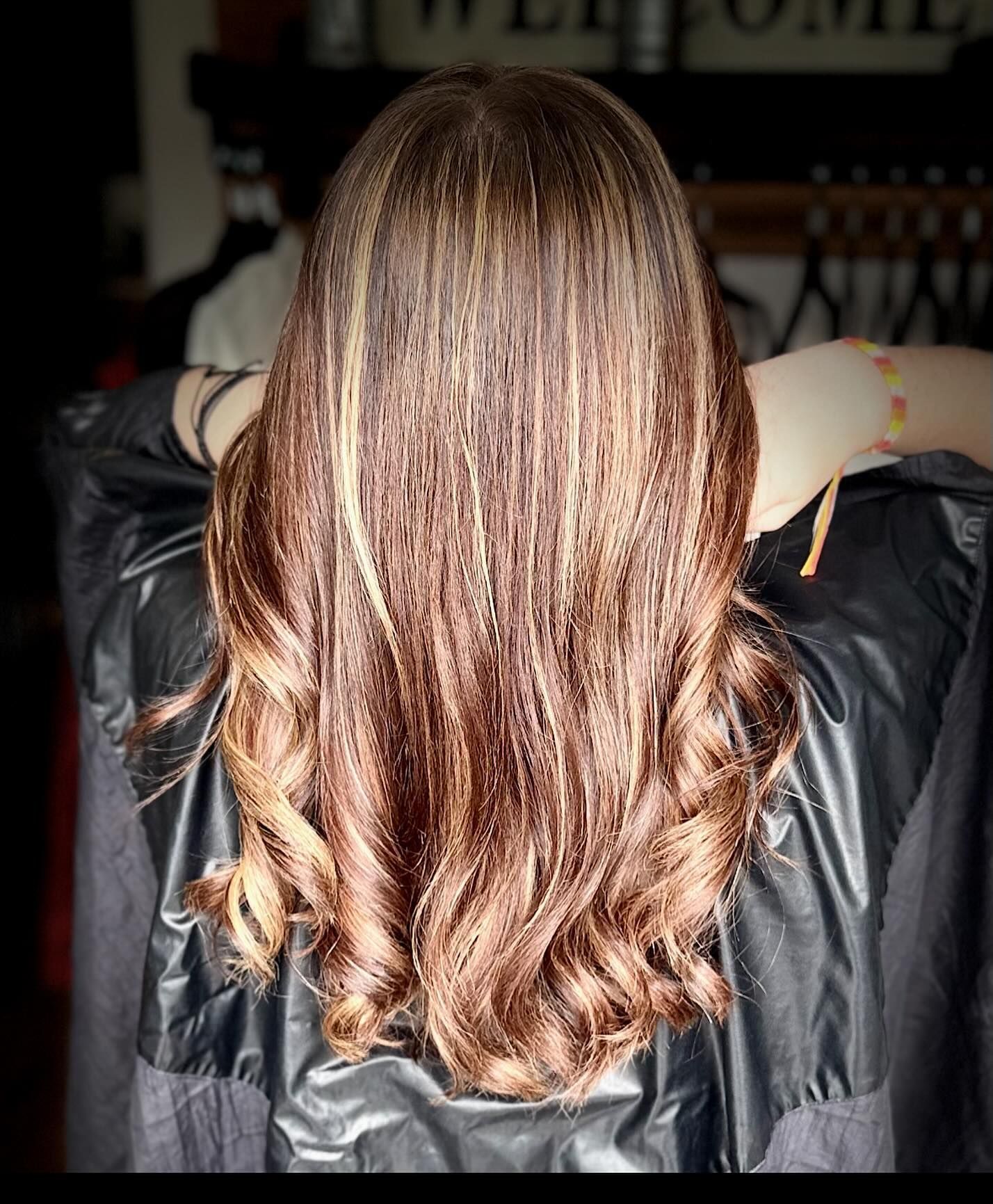 Woman with long, wavy brown hair with blonde highlights, styled at a salon.