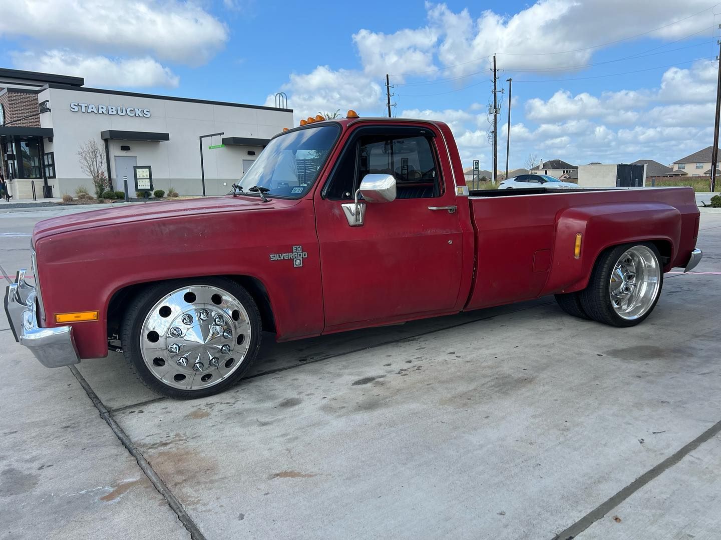 A red truck is parked in a parking lot in front of a building.