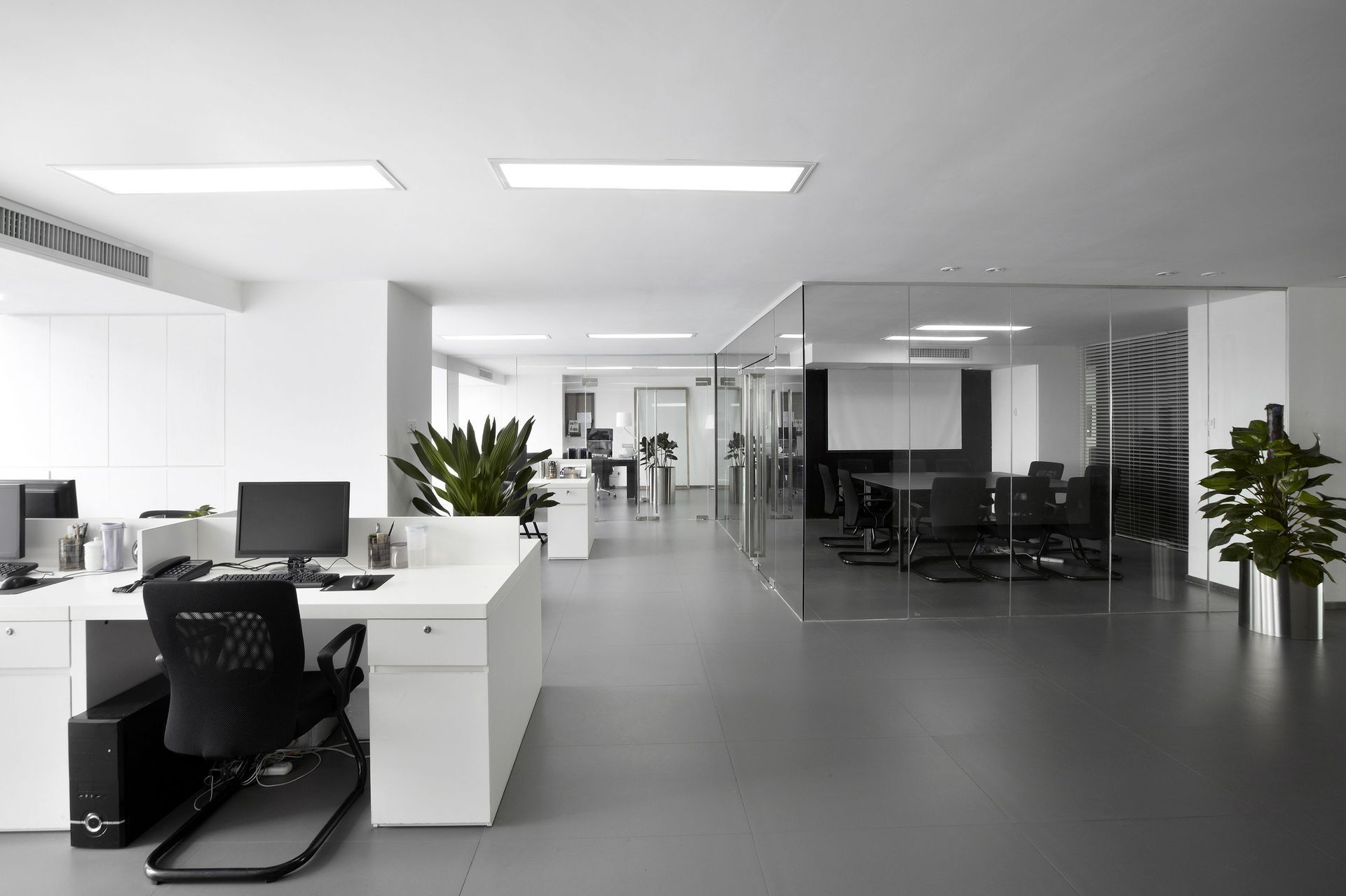 Modern, minimalist office space with white desks, gray floor, glass walls.