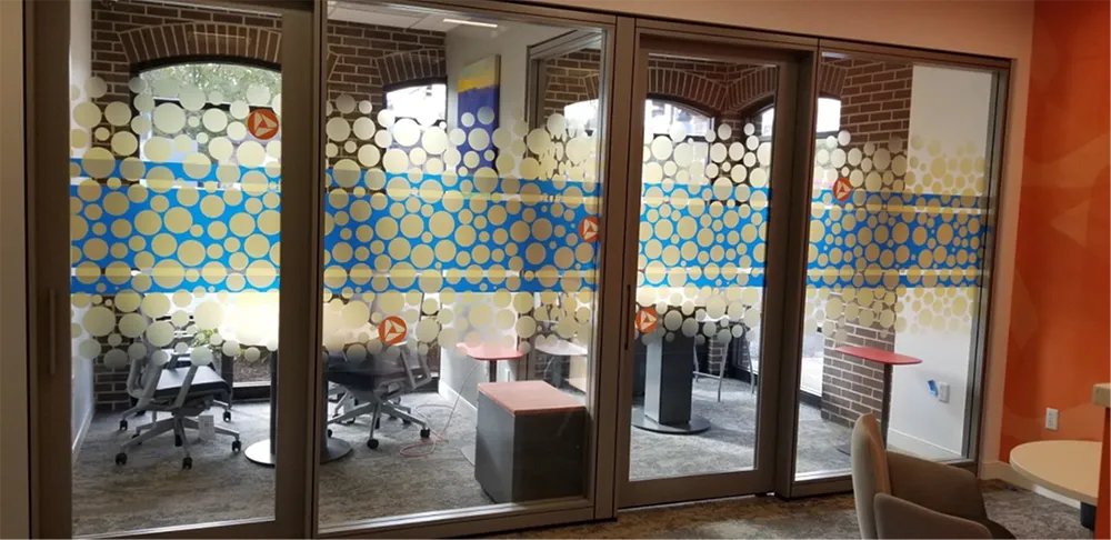 Glass-walled office with decorative patterns. The interior has chairs, tables, and exposed brick.