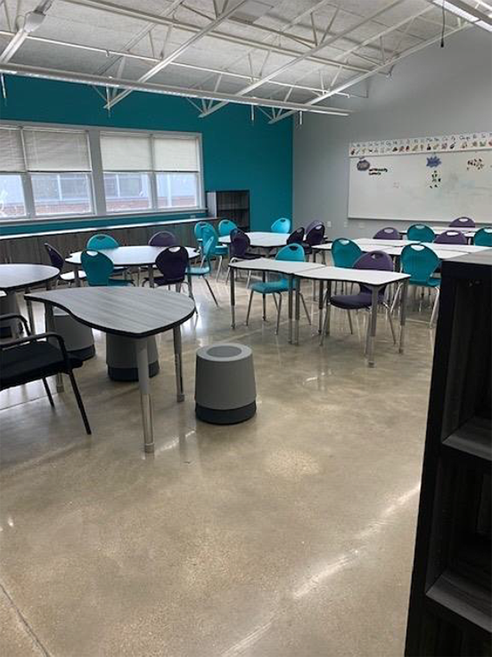 Empty classroom with turquoise and purple chairs, white tables, and polished concrete floor.