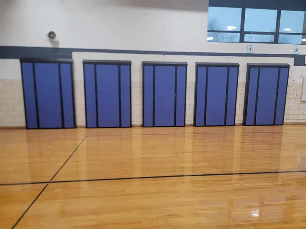 Blue padded wall panels in a gym, mounted on a light wood floor.