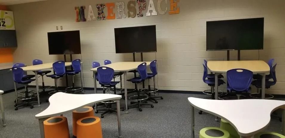 A classroom with tables, chairs, large screens and a 