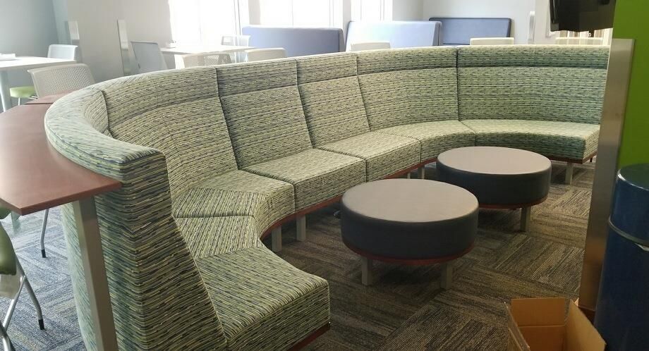 Curved green and gray sectional sofa with two round tables in a public seating area.