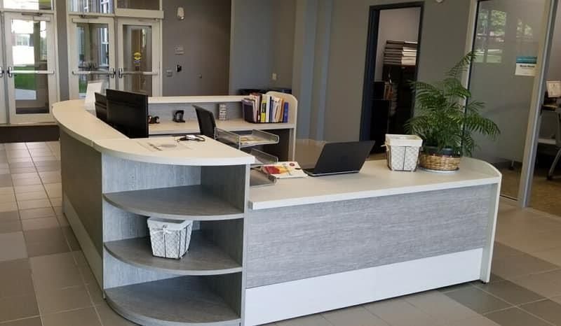 Reception desk in an office lobby with a laptop, potted plant, and shelves.