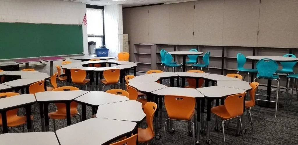 Classroom with round tables, orange and teal chairs, and a green chalkboard.