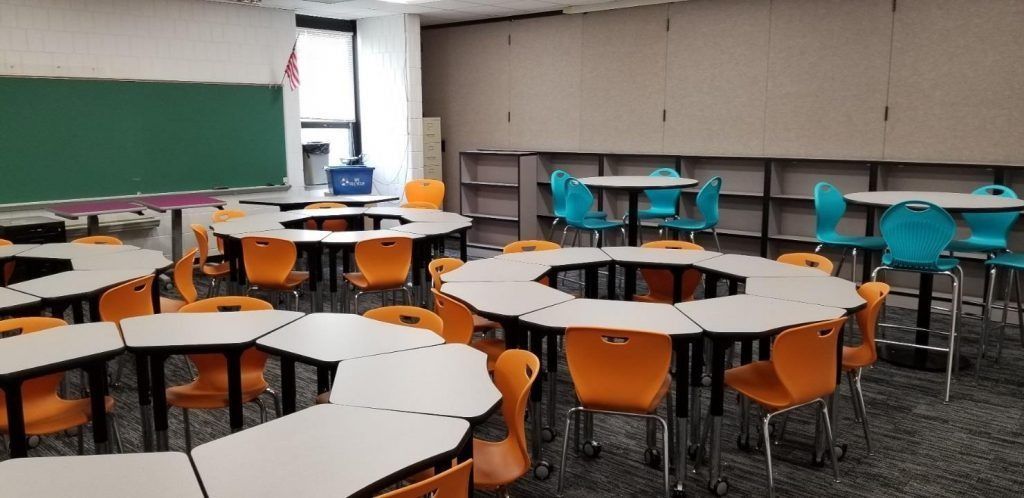 Classroom with round tables, orange and teal chairs, and a chalkboard.