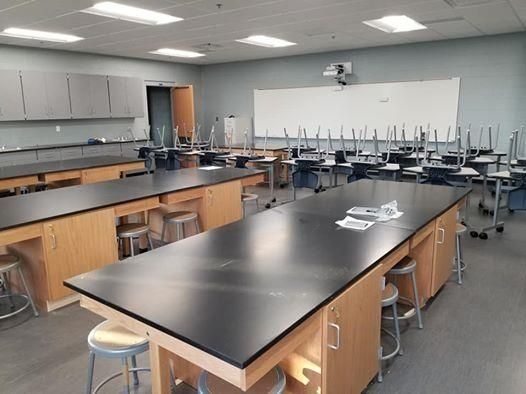 Empty science classroom with lab tables, stools, and wall-mounted storage.