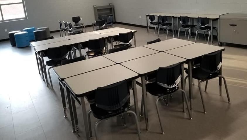 Empty classroom with desks arranged in rows, blue ottomans, and a window.