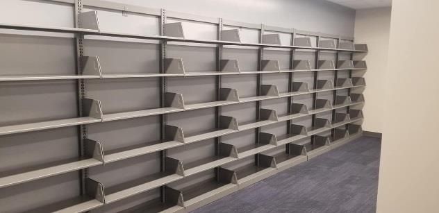 Empty metal shelves built into a wall, in a room with carpet and a plain wall.