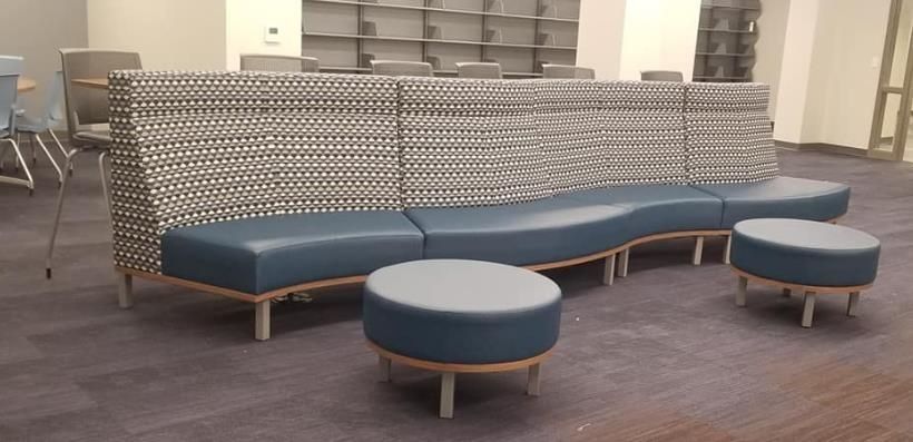 A modern curved blue sofa with patterned back and two matching ottomans in a room.