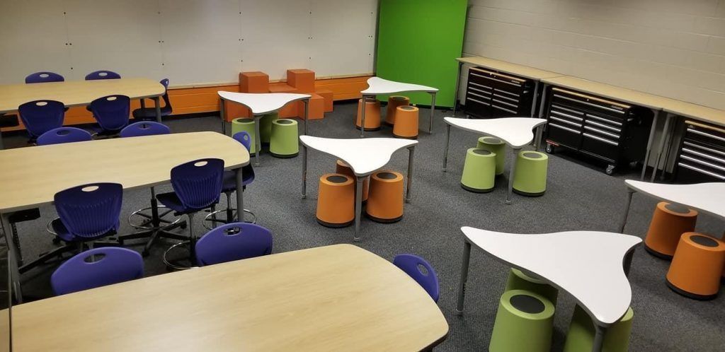 A classroom with student tables, chairs, and colorful round seats. Some tables have students with blue chairs.