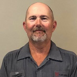 Bald man with a mustache, wearing a gray collared shirt. He&rsquo;s smiling slightly, in front of a neutral background.