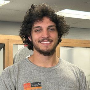 Man with curly dark hair and goatee smiles at the camera, wearing a gray t-shirt.