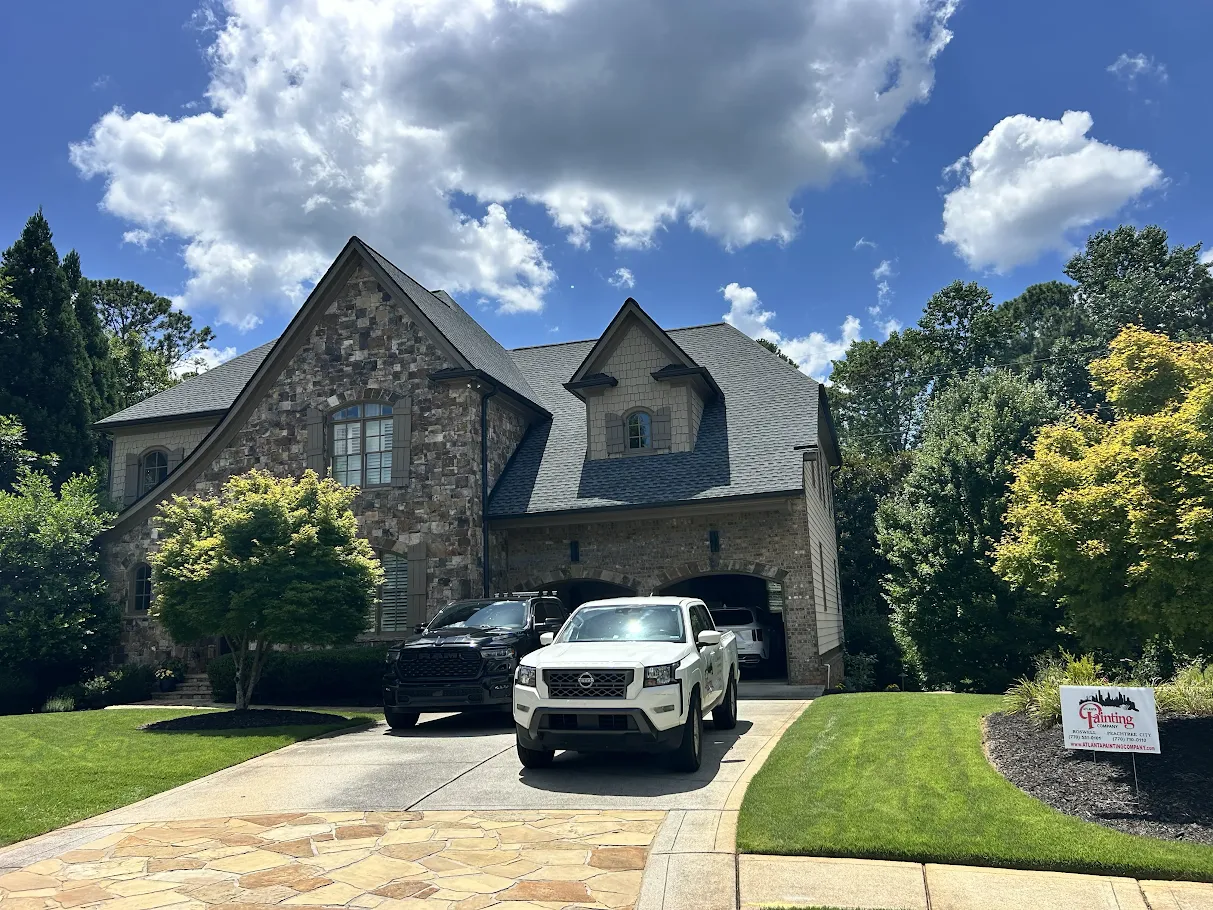 Stone house with a two-car driveway, black SUV and white truck, under a bright blue sky with clouds.