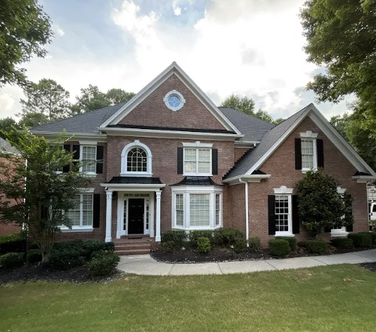 Large brick suburban house with white trim, front porch, and manicured lawn under a cloudy sky