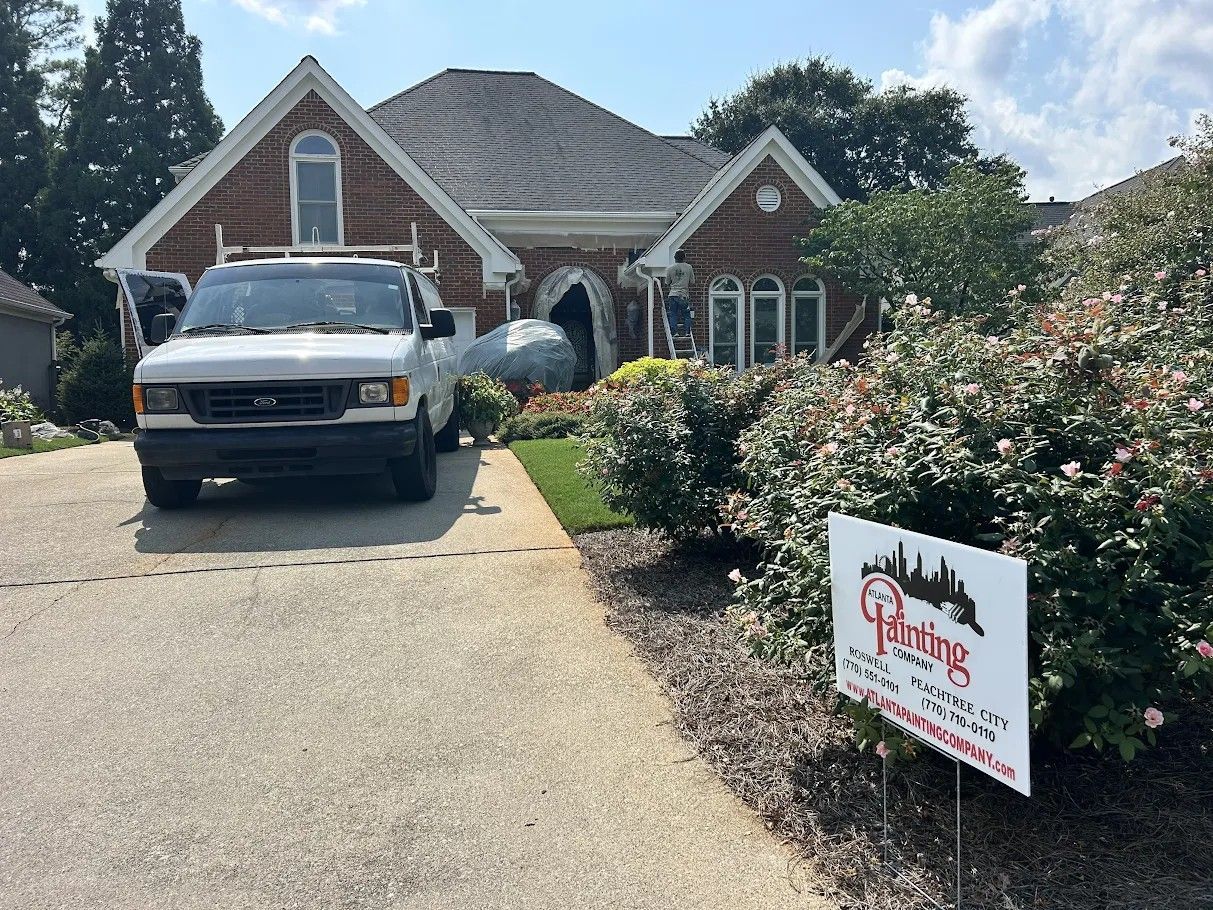 White pickup truck in a brick house driveway with a lawn sign for Atlanta Painting Company on the right.
