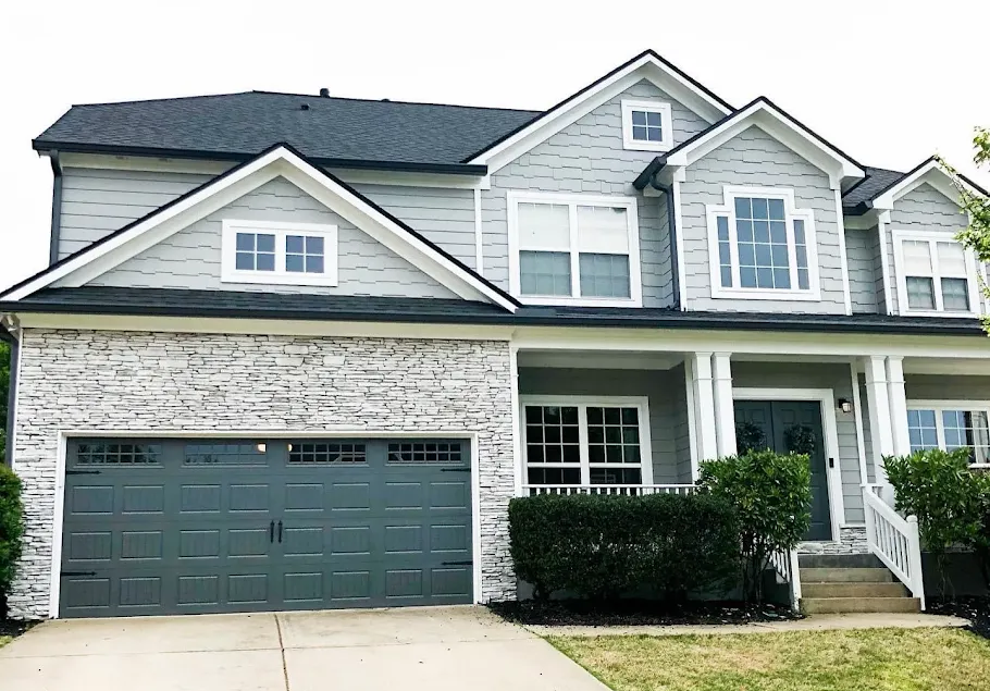 Two-story suburban townhouse with gray siding, stone façade, and dark garage doors.
