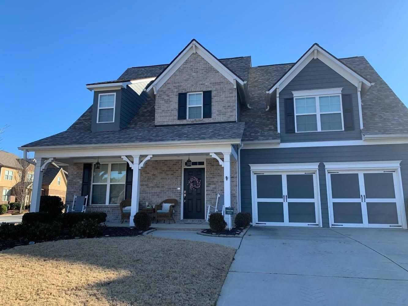 Two-story house with blue-gray siding, brick, and a two-car garage; clear sky.