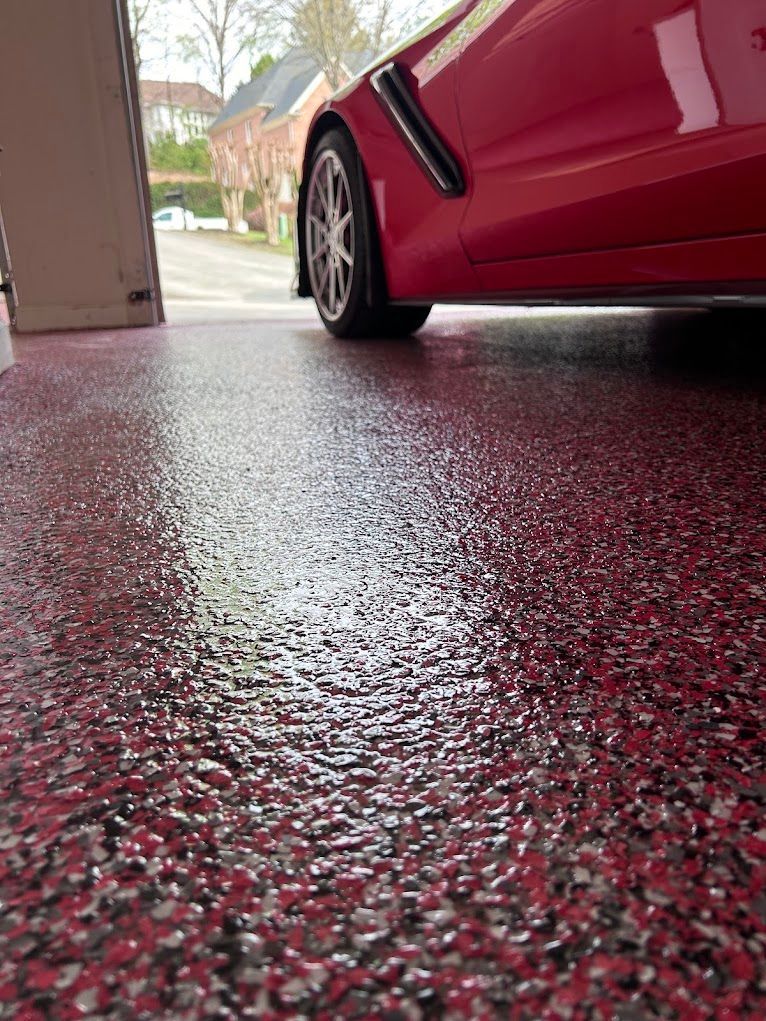 Red sports car in a garage with a speckled red, gray, and white epoxy floor. The garage door is open.