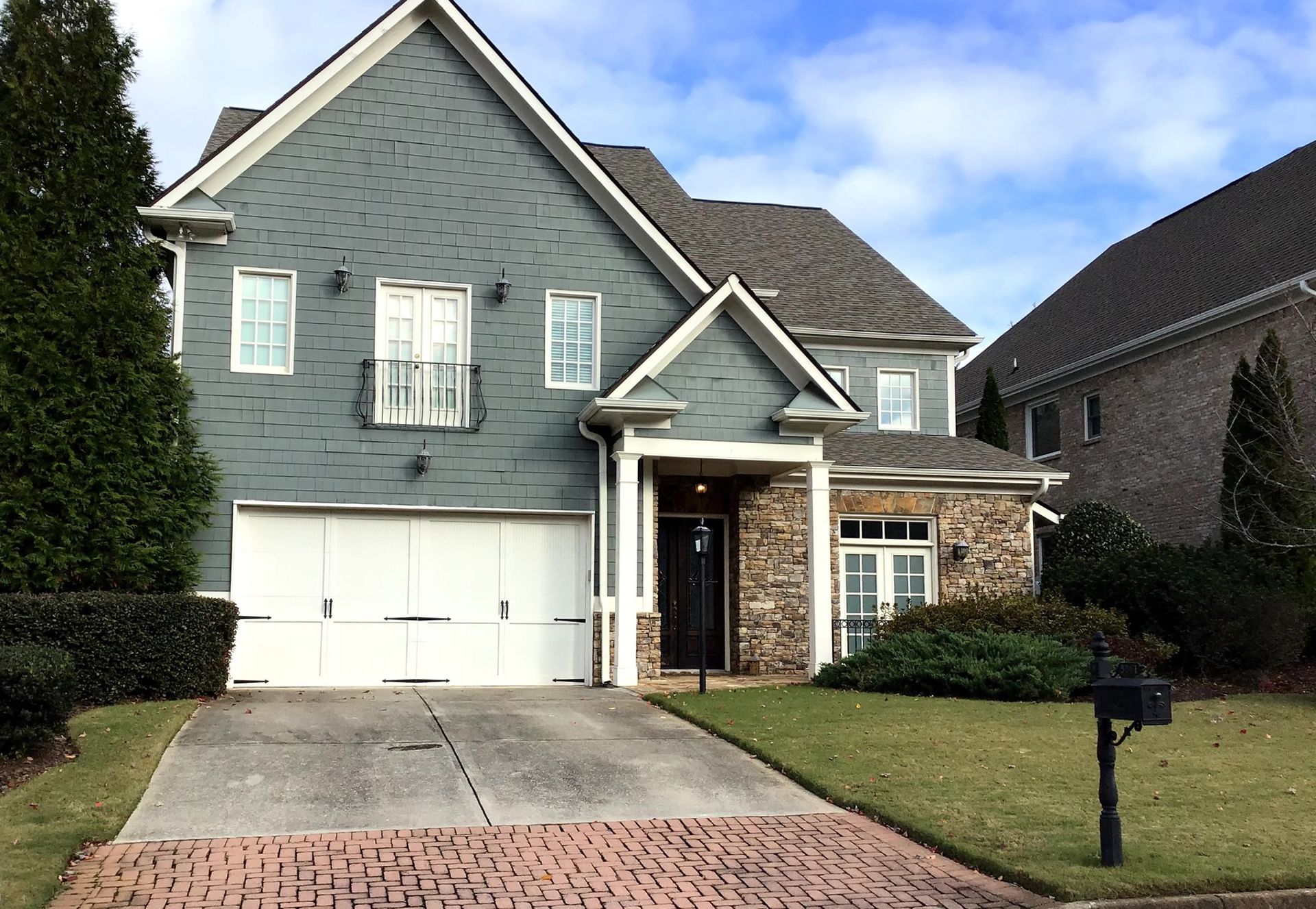 Two-story house with blue siding, brick accents, white garage door, and a small porch.