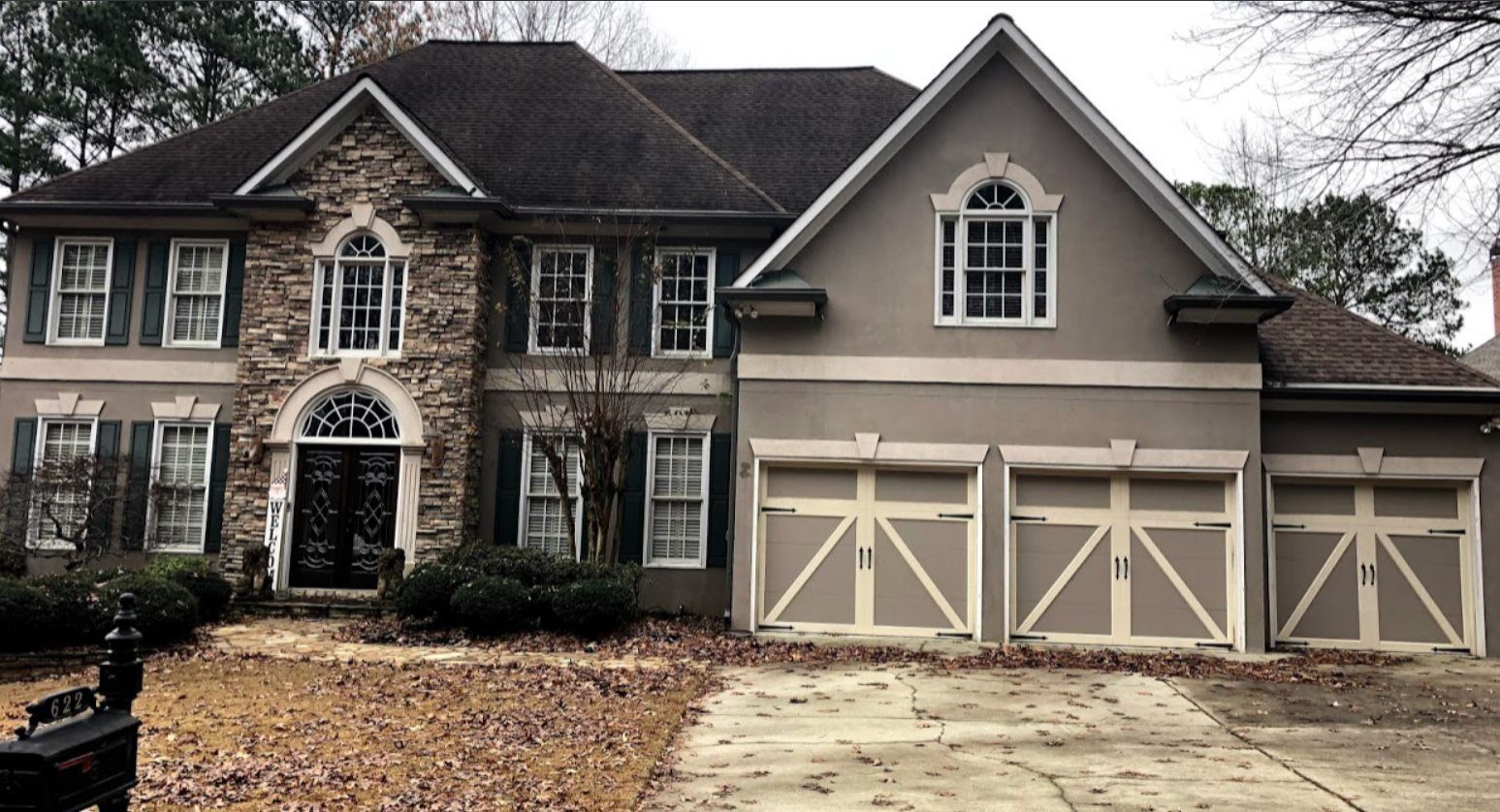 Two-story home with stone and beige facade, three-car garage, and black front door.